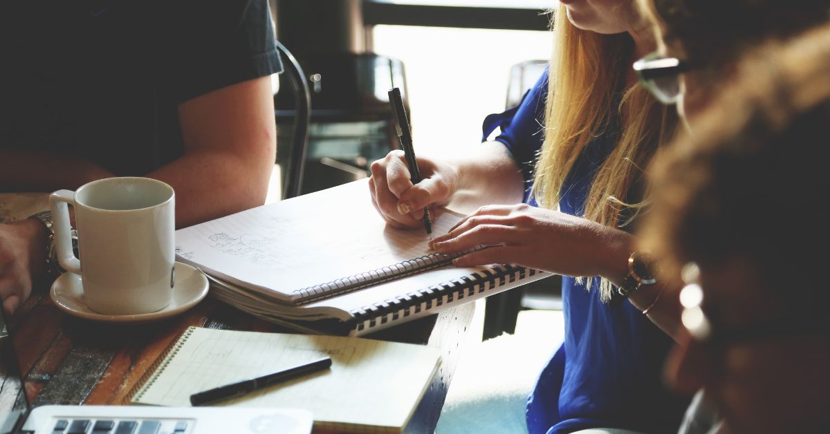 A girl with other guys in an office writing on her notebook