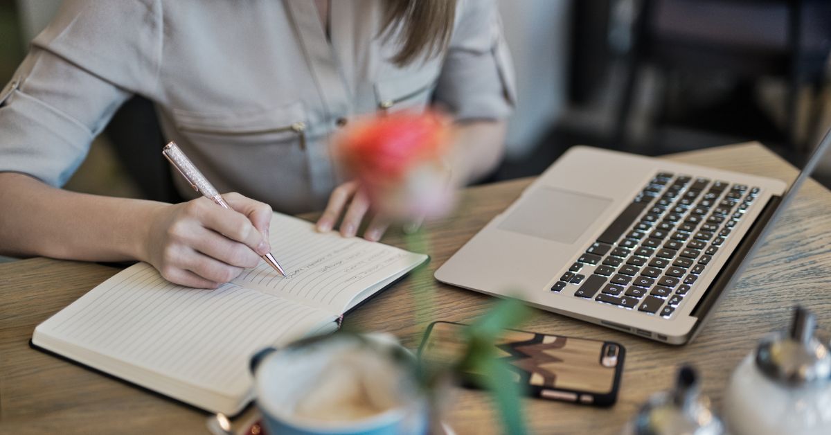 a girl writing on her notebook on a desk with her stuff
