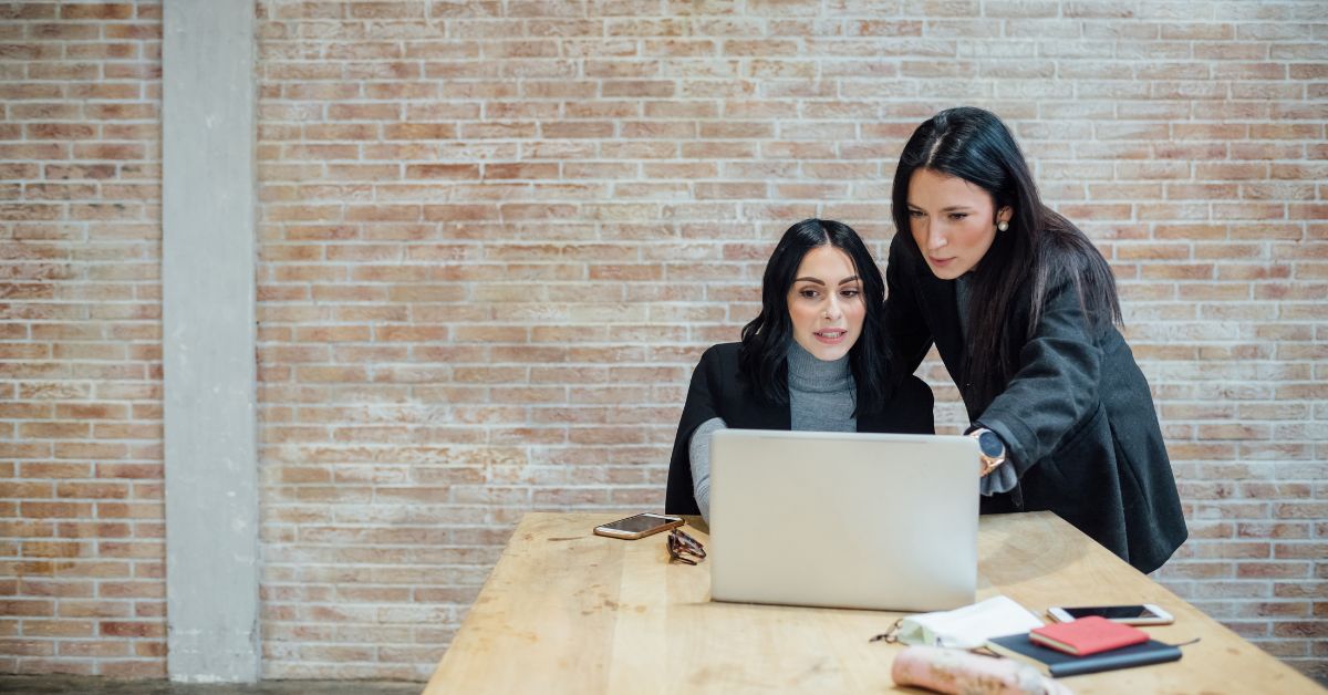 two ladies looking at a laptop in a brick walled room