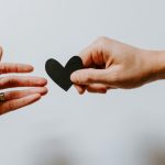 ALT TEXT: Two people exchanging a paper cut heart via Unsplash.com